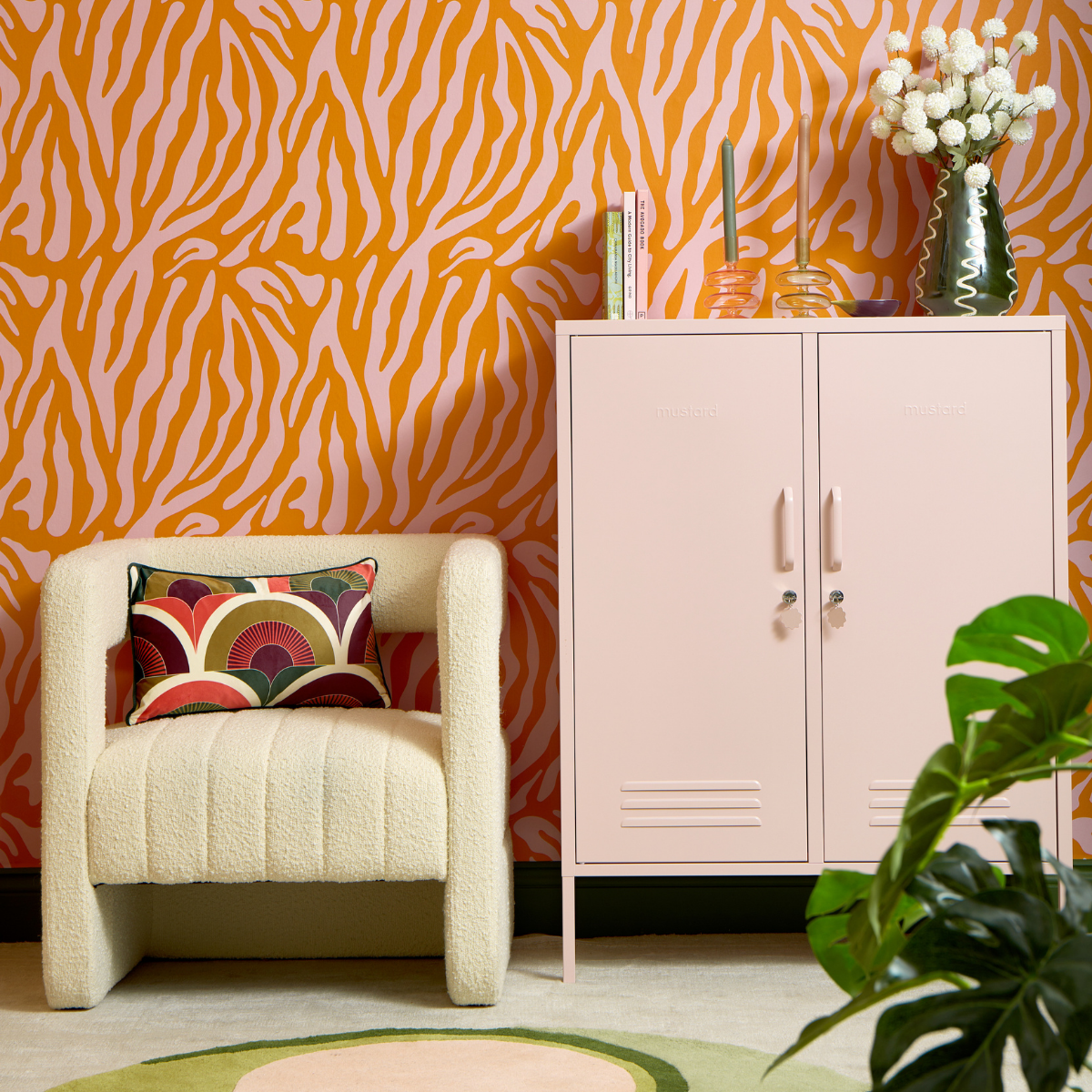 A Blush Midi sits against pink and orange zebra patterned wallpaper. There is a cream boucle chair next to the locker.