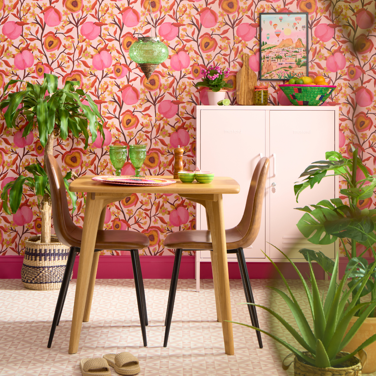 Vibrant green plants surround a small table and chairs. There is a Blush Midi standing against an intricate peach patterned wallpaper.