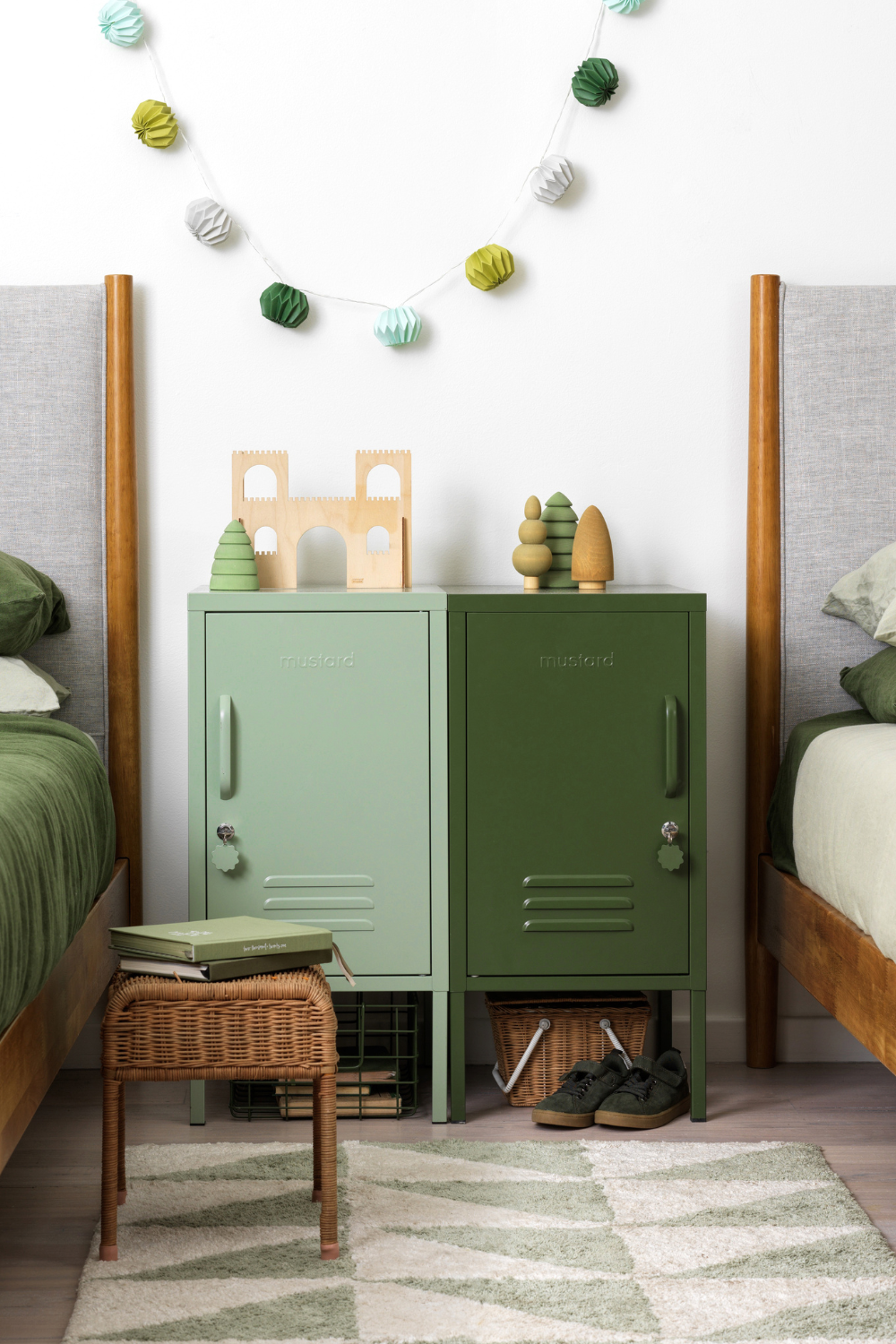 Two Shortys in Sage and Olive sit side by side in a kids bedroom. They are positioned between two beds dressed in green linens and there is a green paper garland hanging on the wall.