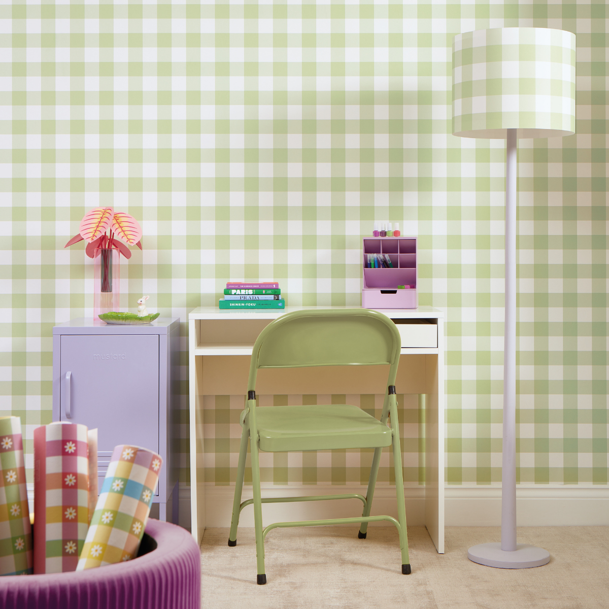 A pastel workspace features a Lilac Shorty with pea green gingham wallpaper and a matching lamp. There is a small white desk and a green folding chair.