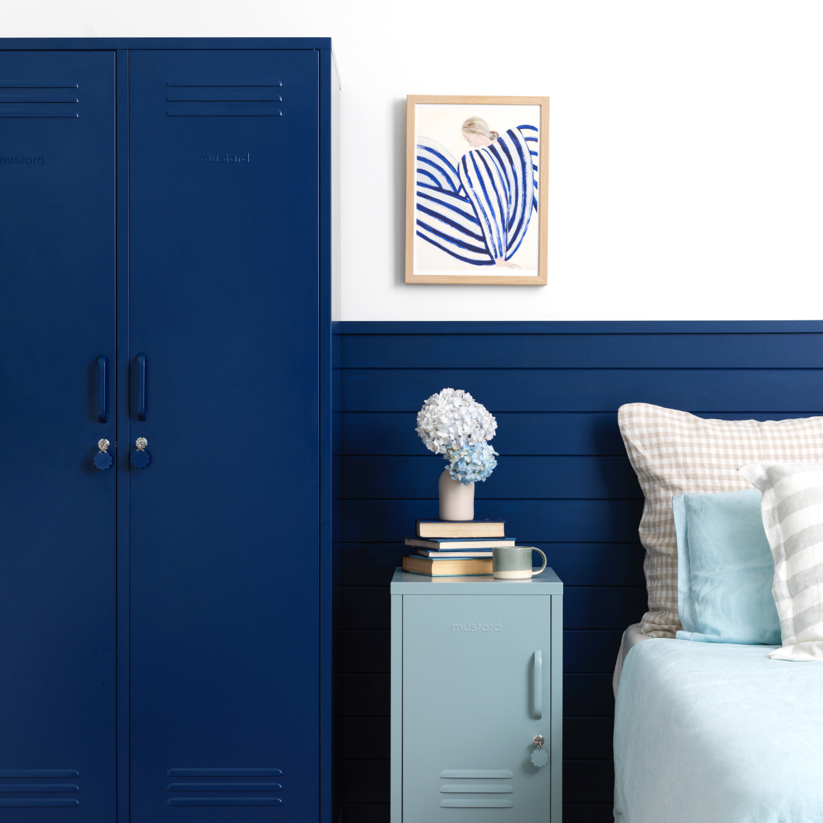 An Ocean Shorty acts as a bedside table beside a bed dressed in blue and white linens. There is a Navy Twinny next to the Shorty and the wall behind is painted in a matching shade of Navy.