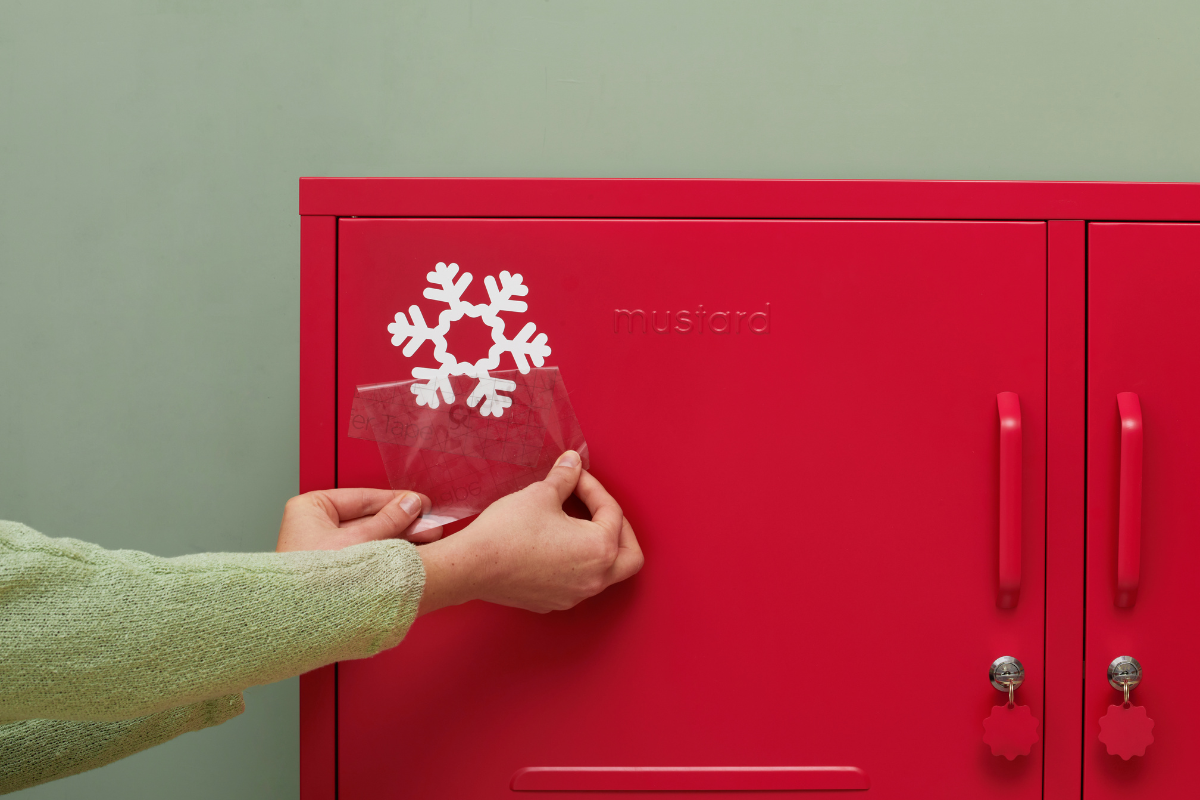 A person is peeling off the Transfer Tape revealing a snowflake decal on a Mustard Made logo.