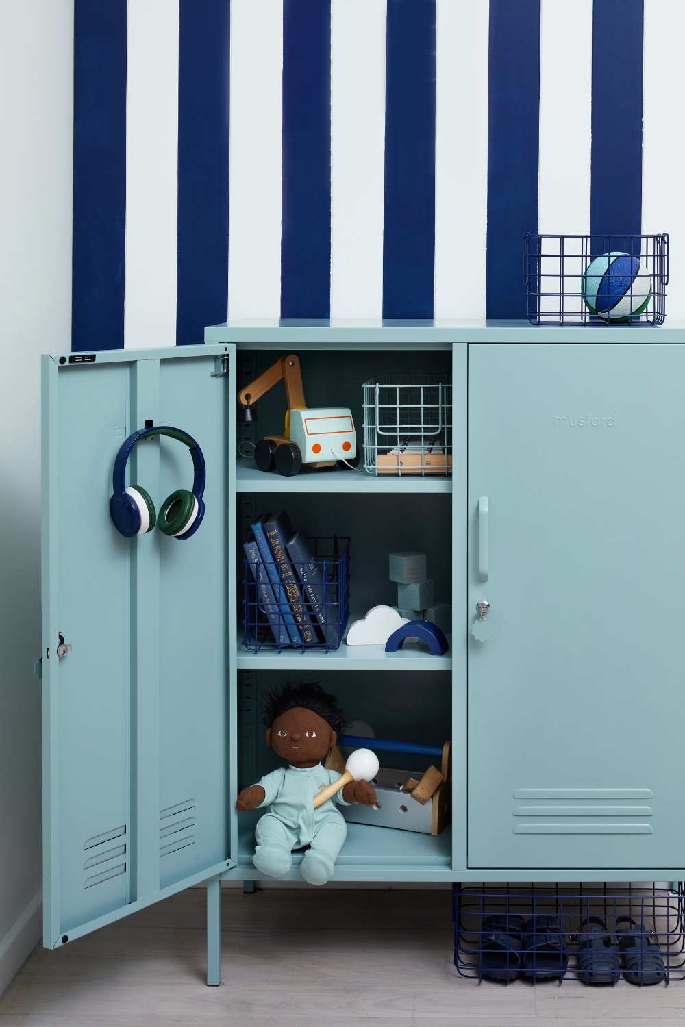 An Ocean Midi sits against a navy and white striped wall. One of the locker doors is open, displaying a collection of child's toys including a doll, fire truck and books.