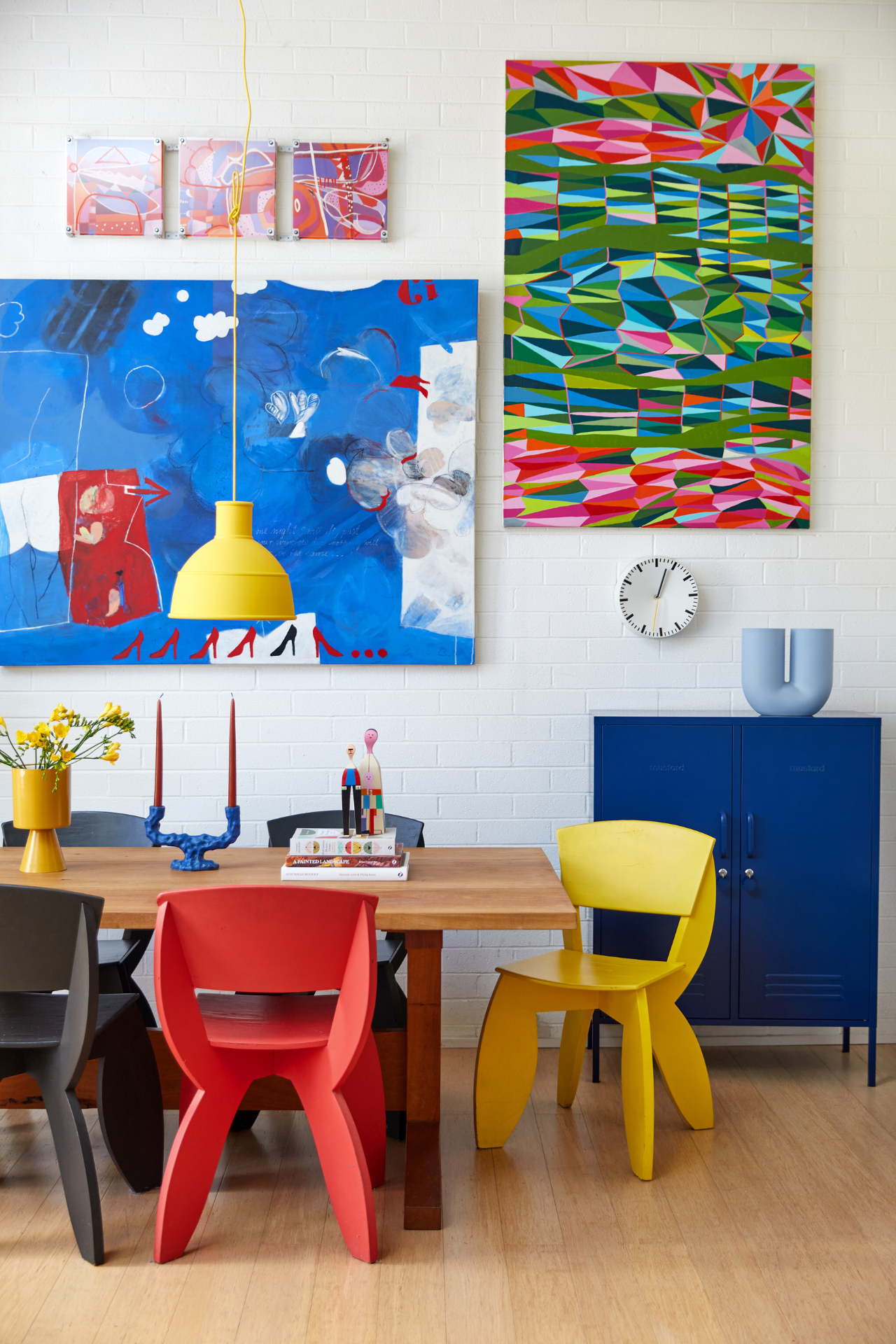 A close up of a dining table with large, brightly coloured artworks on the wall behind it.