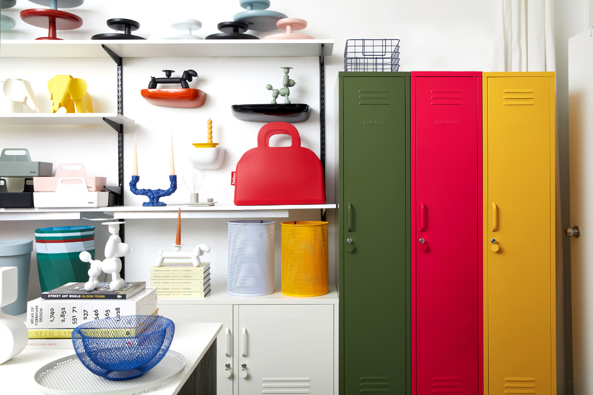 A trio of tall skinny lockers in red, olive and yellow stands out against a collection of bright design objects on white shelving.