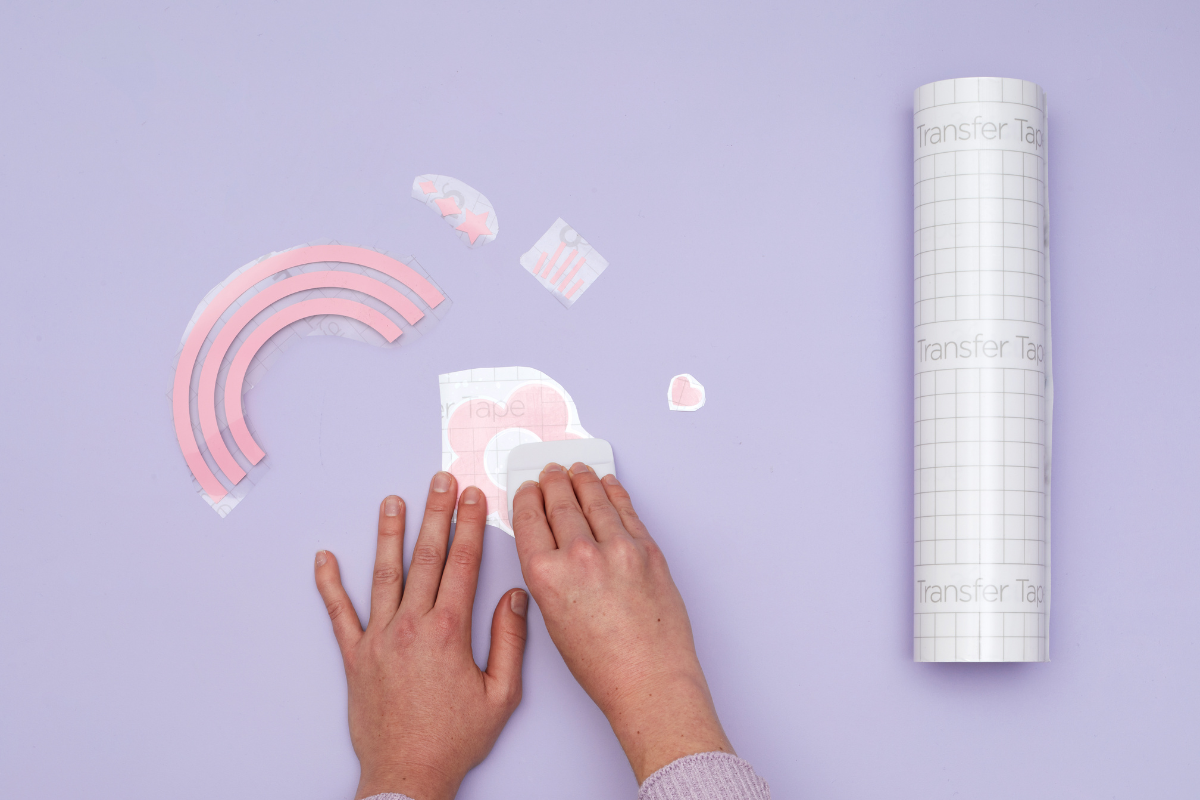 A close up of hands applying transfer tape over a sticker decal and using the scraping tool to remove any air bubbles.