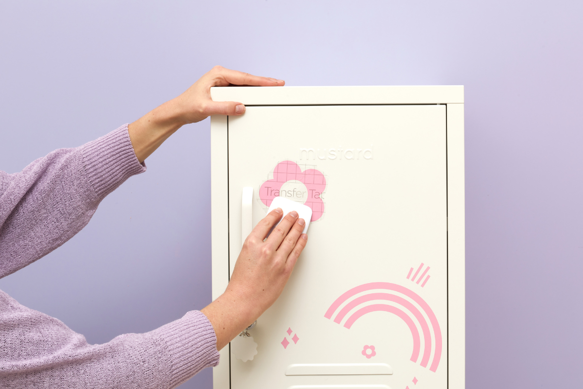 A close up of a person wearing a lilac jumper and applying decals to the front of a locker.