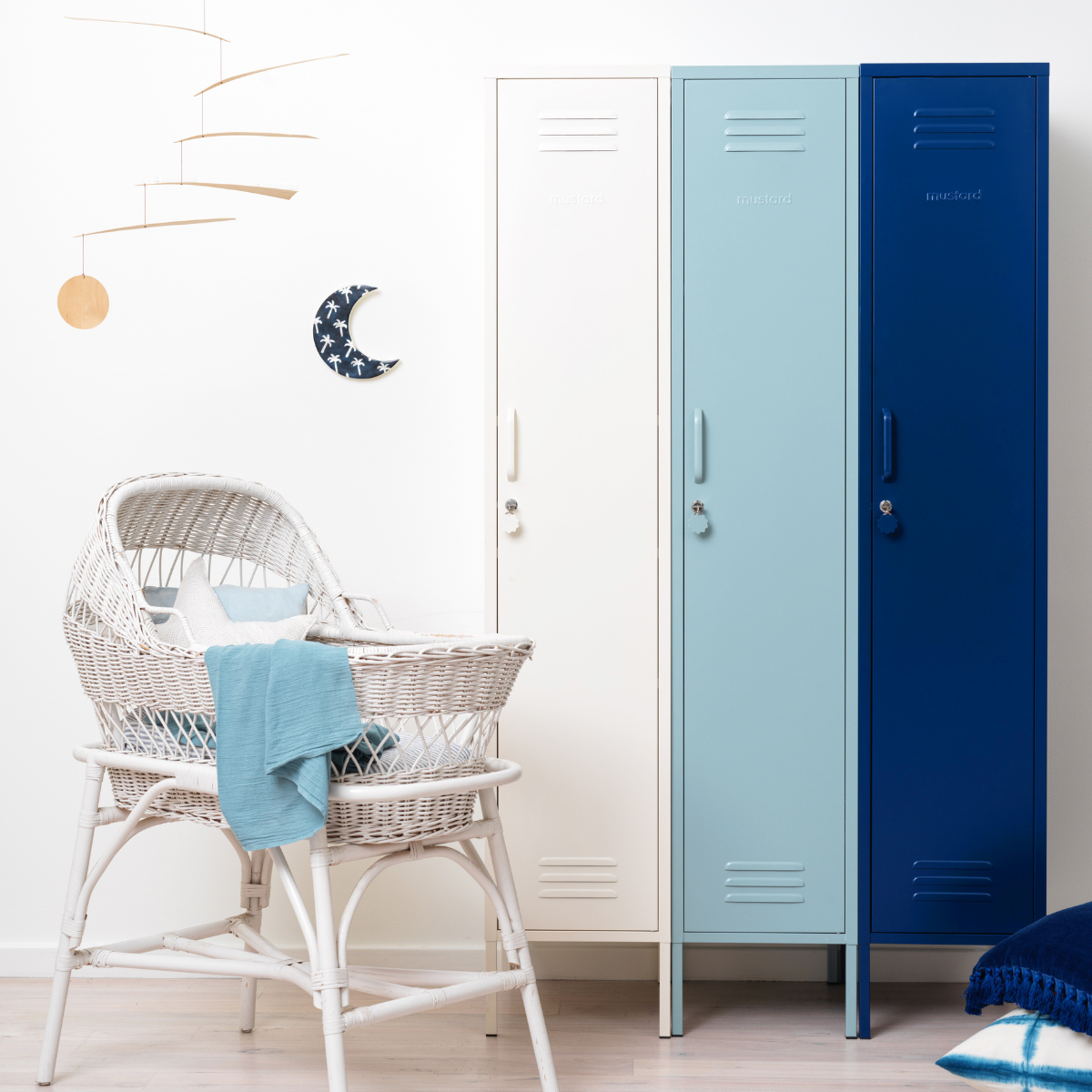 A trio of Skinny lockers in an ombre of White to Ocean to Navy sit behind a white wicker bassinet.
