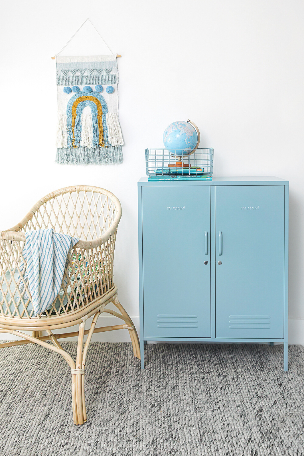 An Ocean Midi sits next to a rattan bassinet in a blue-themed nursery. There is a tufted wall hanging and a collection of Ocean blue accessories.