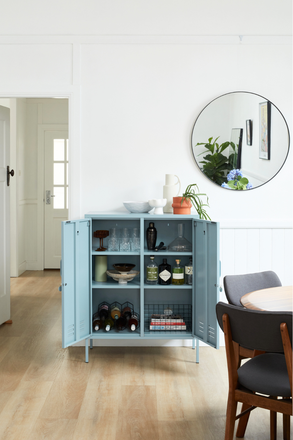 An Ocean Midi sits in a living space with its doors open. Inside bar accessories are styled up, including bottles of alcohol, glasses and serveware. There is a collection of ceramics sitting on top of the locker.