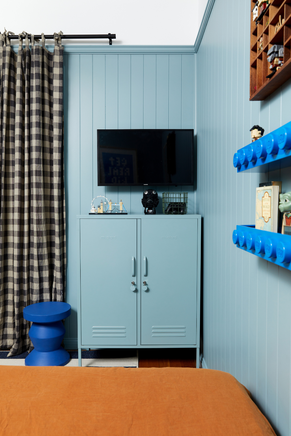 An Ocean Midi is styled in a teenager's bedroom with matching Ocean coloured walls. There is a TV mounted above it and lego shelving on the walls.