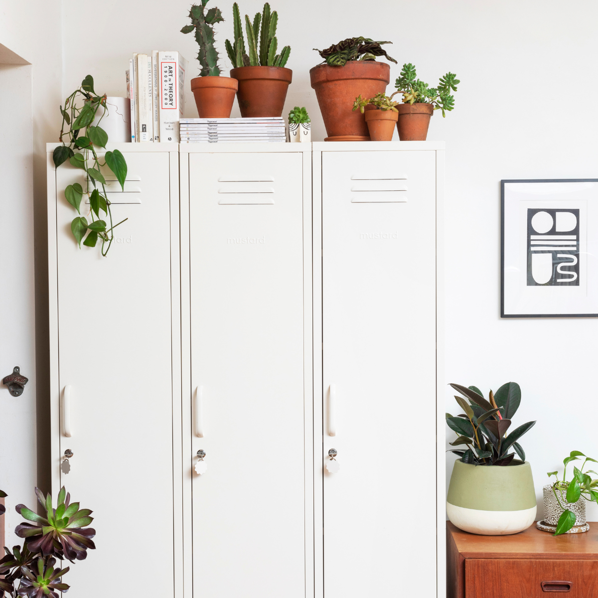 Three Mustard Made Skinny lockers stand side by side. They are all the colour, White. There are terracotta pots with green plants sitting on top, as well as stacks of magazines. 