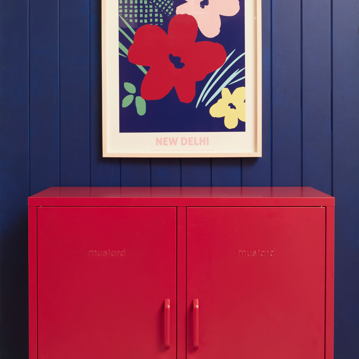 A Poppy Midi sits against a Navy wall with a blue and red floral print hung above.