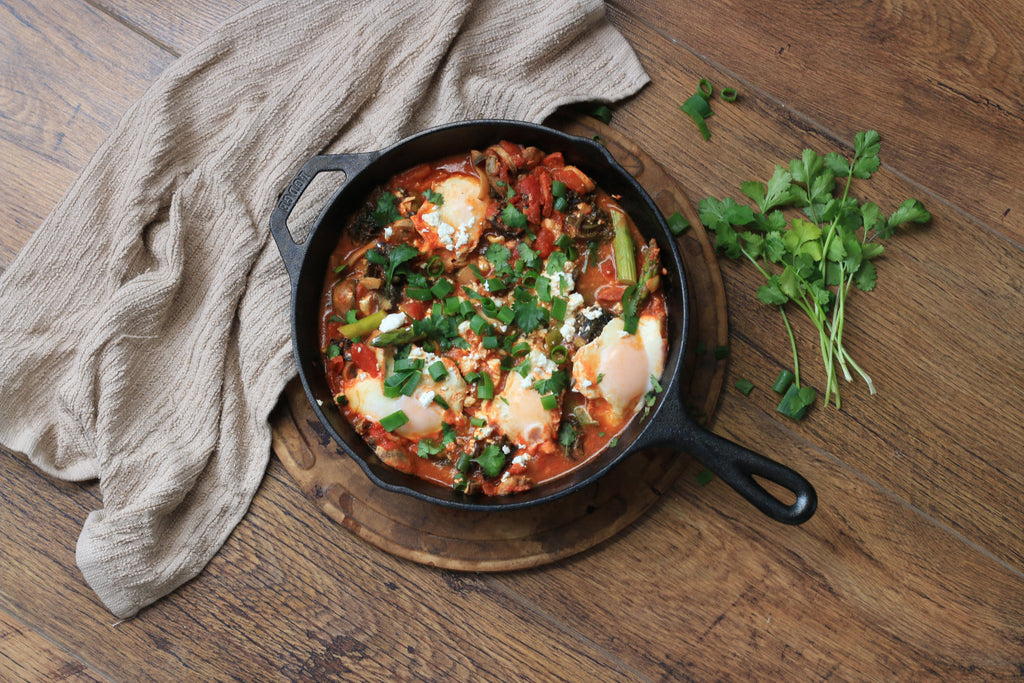 Cast iron skillet with egg and chorizo breakfast scramble on a table with a towel and cilantro next to it