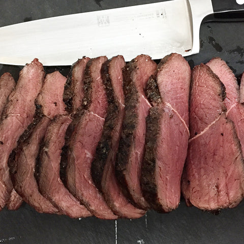 Seared medium-rare venison roast sliced to perfection with the knife pictured above it