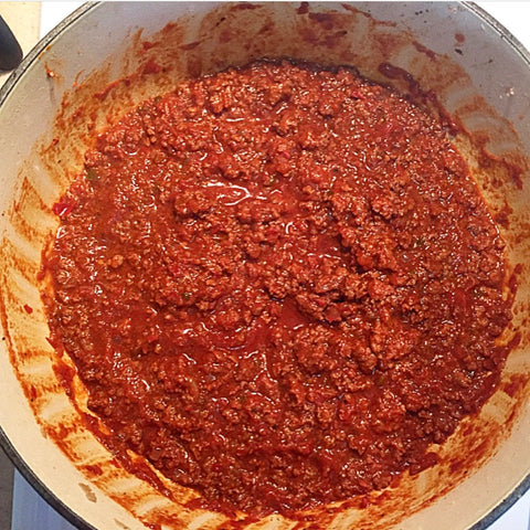 Venison chili being stirred in saucepan to prevent scorching