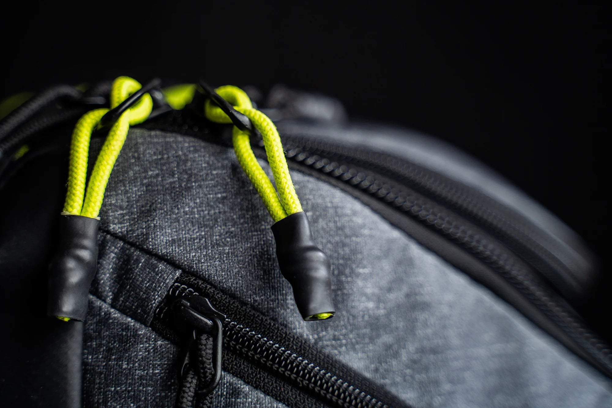 Close-up of a gray zipper with bright green pull cords on a backpack.