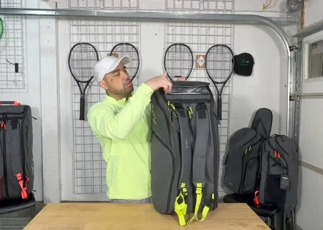 Man in garage examining tennis bag among rackets.