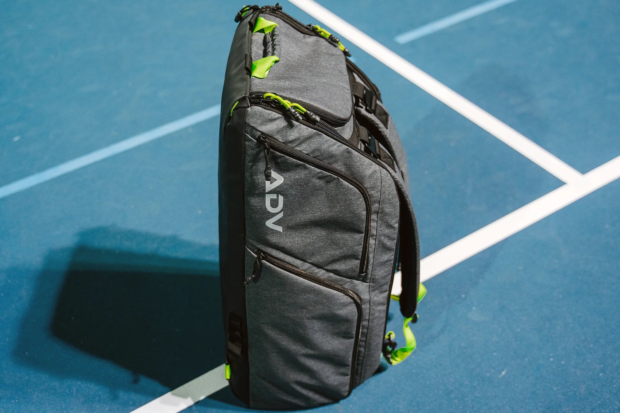 Gray backpack standing upright on a blue sports court.