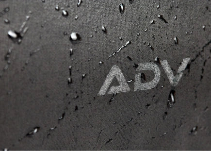 Close-up of dark fabric with water droplets and ADV logo.