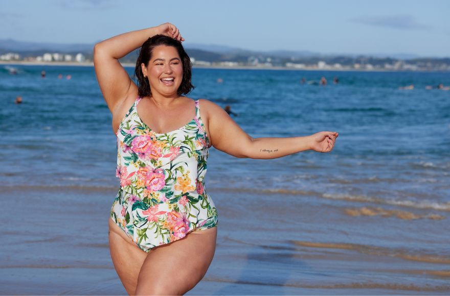 Woman with short brown hair wears white ruffle one piece with pink, orange and green tropical print.