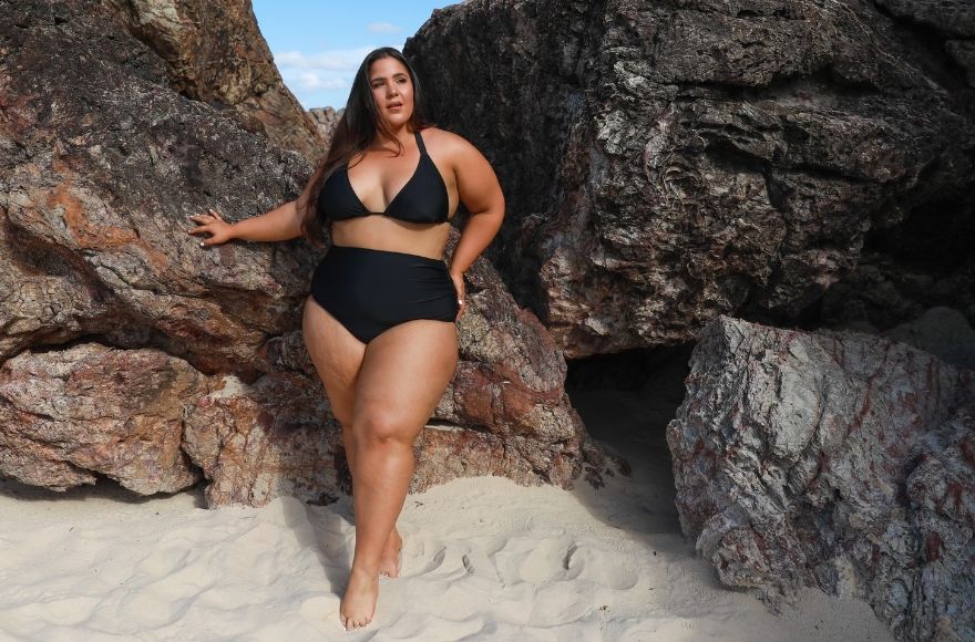 Brunette woman wears black triangle bikini top and high waisted maternity belly pant