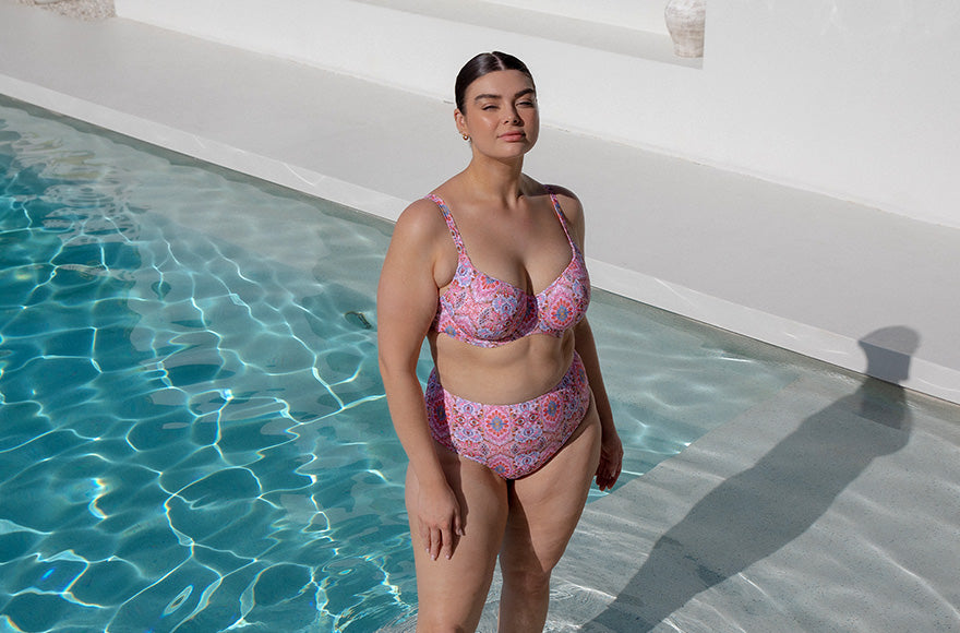 Brunette model standing in a shallow pool wearing a pink patterned bikini