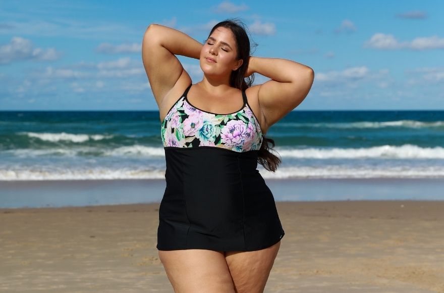 brunette woman poses at the beach wearing Positano Black underwire swim dress
