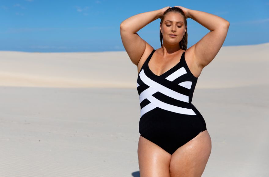 Woman with slicked back hair poses on a beach wearing Acapulco Black and White criss cross one piece swimsuit
