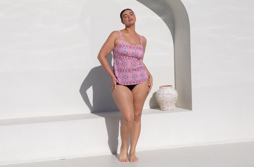 Woman with slicked back brown hair wears pink boho print tankini top with plain black pants