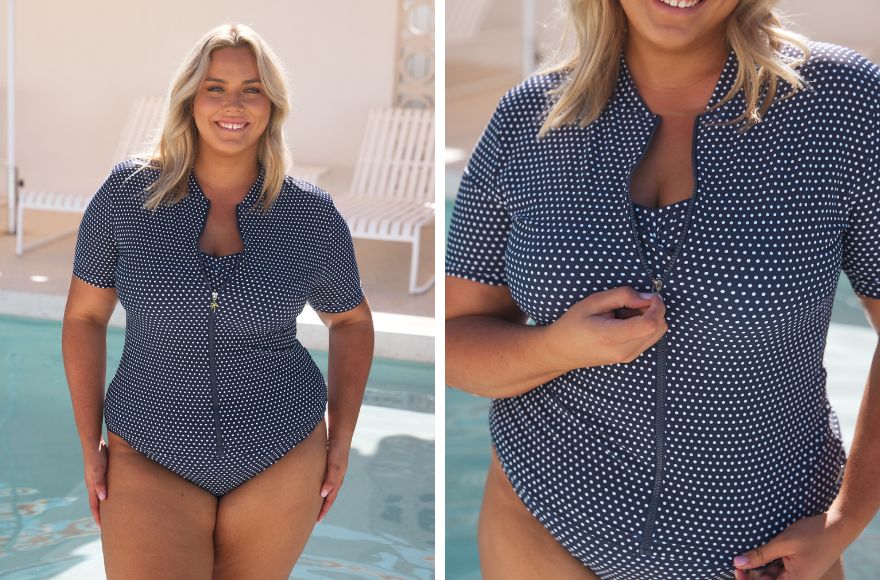 Woman with blonde hair stands by the pool wearing navy and white polka dot one piece swimsuit with matching short sleeve rash vest