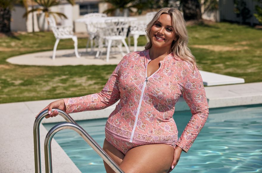 Woman with blonde hair poses in the pool wearing a pink floral long sleeve rash vest and matching bikini