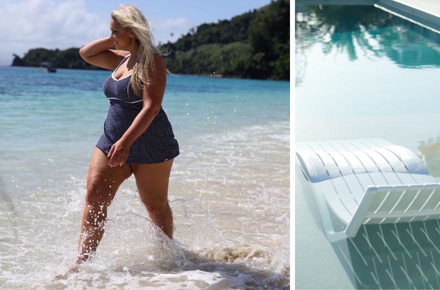 Woman with blonde hair walks along the shoreline wearing navy swim dress with white polka dots