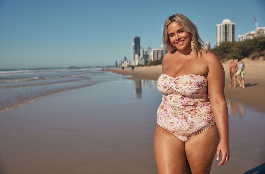 Woman with blonde hair poses at the beach wearing strapless pale pink floral one piece