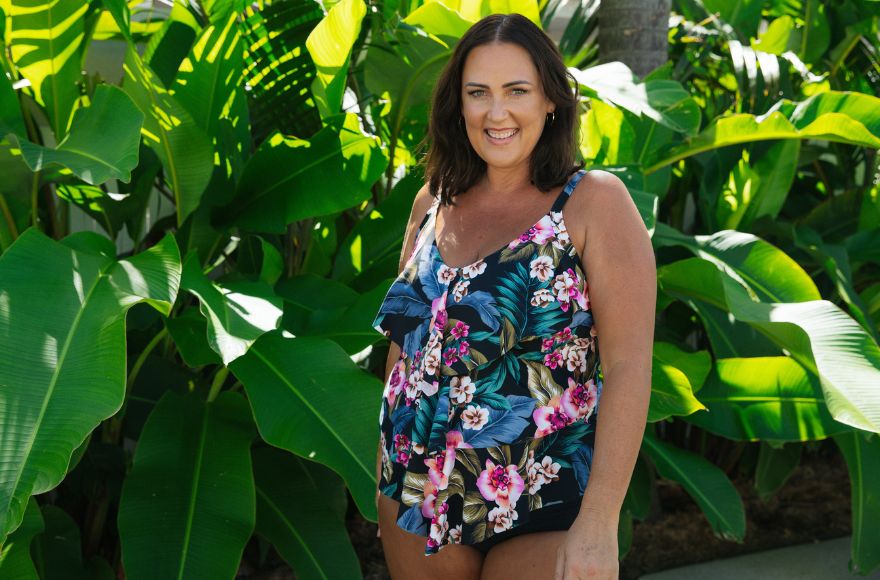 Woman with brown hair wears ruffled tankini top with bright tropical print