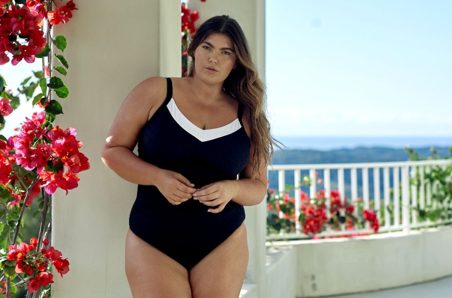 woman with long brown hair wears black underwire one piece swimsuit with white trim around the neckline