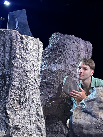 Zack holding up a small robotic rock, surrounded by large robotic rocks, on the set of ‘Sacrifice’ by Robert Walton