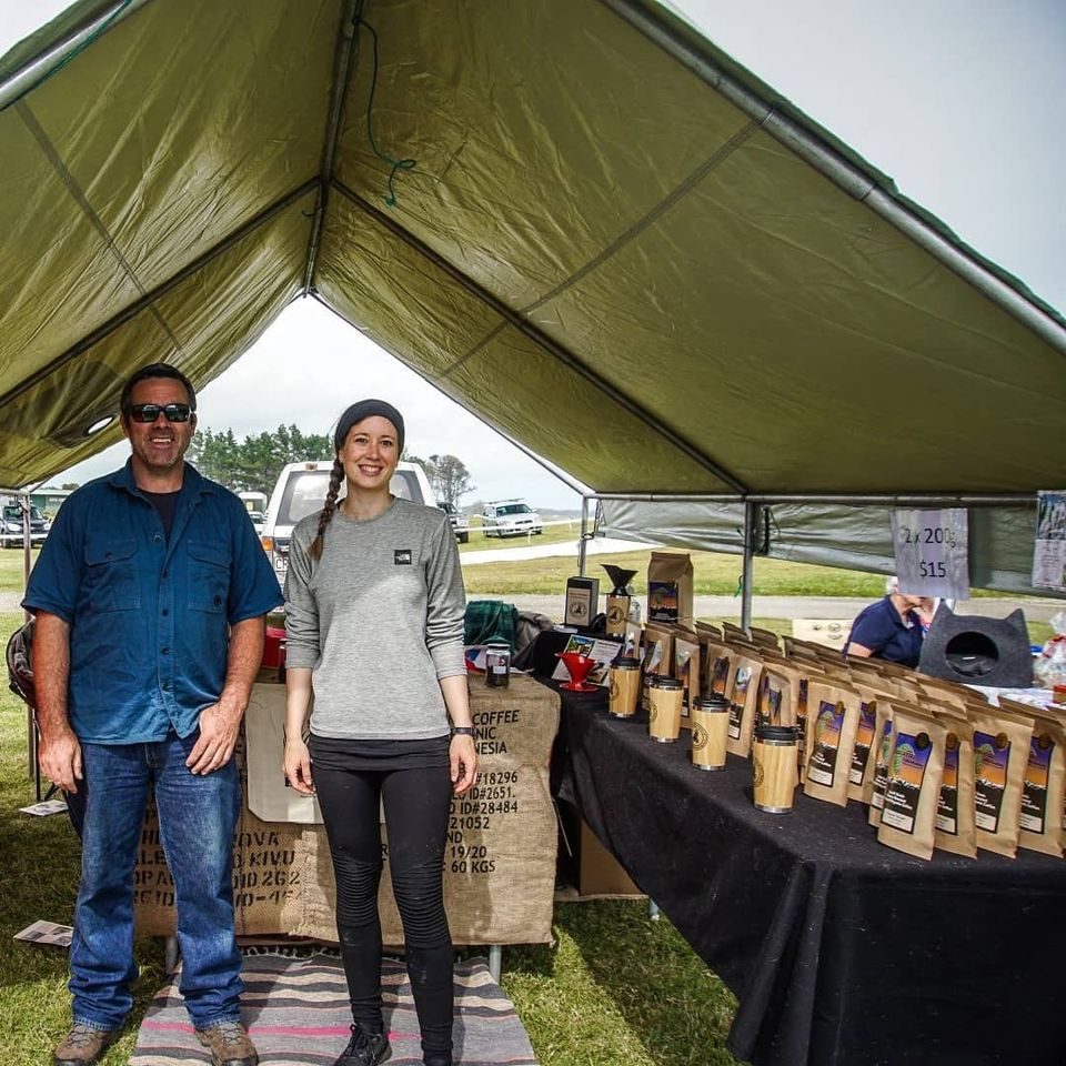 Buck & Avi standing in a green tent at a market, surrounded by their coffee.