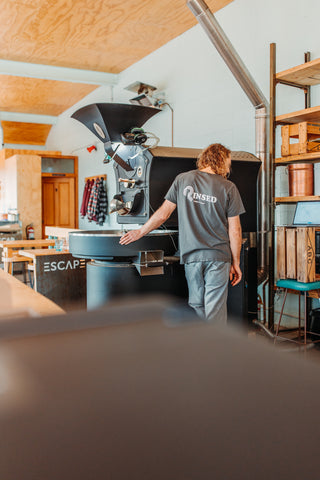 Image of a coffee roasting machine in the distance with the head roaster leaning against it.