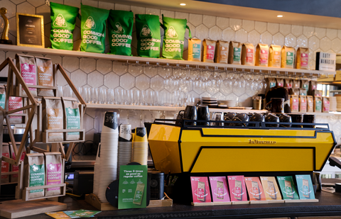 A big yellow coffee machine sits on the cafes front desk with a rainbow of colourful Common Good Coffee bags on a shelf in the background