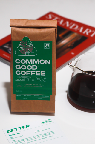 A bag of Common Good Coffee, the better blend is sitting next to a pour over jug of filter coffee. A tasting card for the Better Blend sits in front.