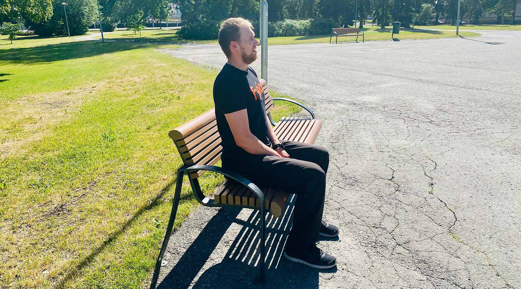 Mies istuu suoraselkäisesti puistonpenkillä kesäisessä säässä