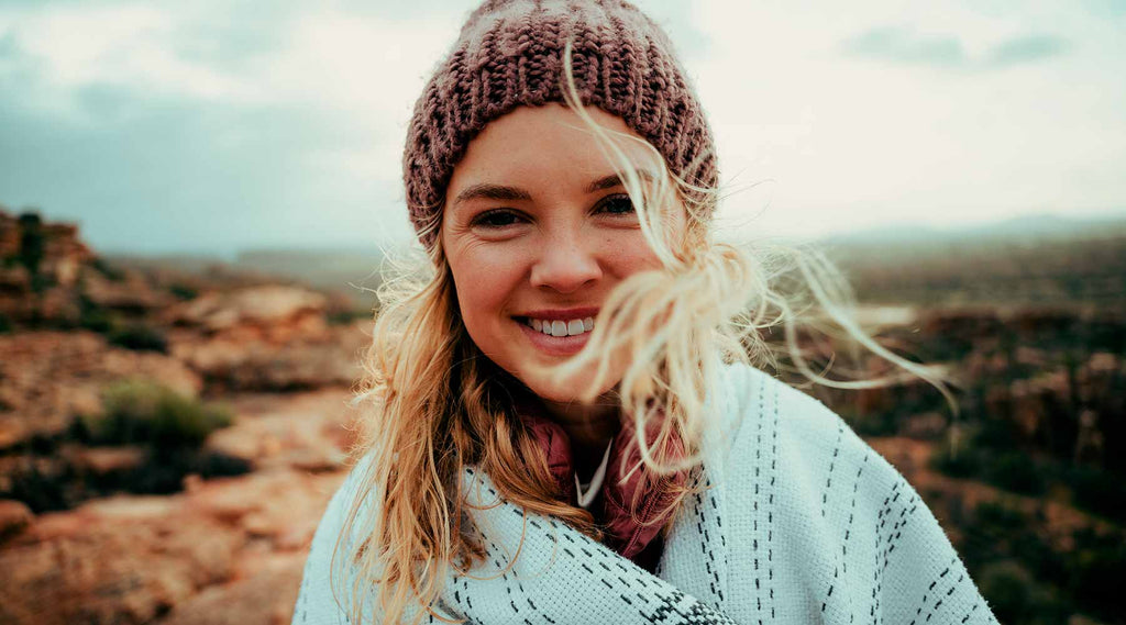 Nainen hymyilee onnellisesti vuoristossa syksyisessä säässä päällään talviset vaatteet
