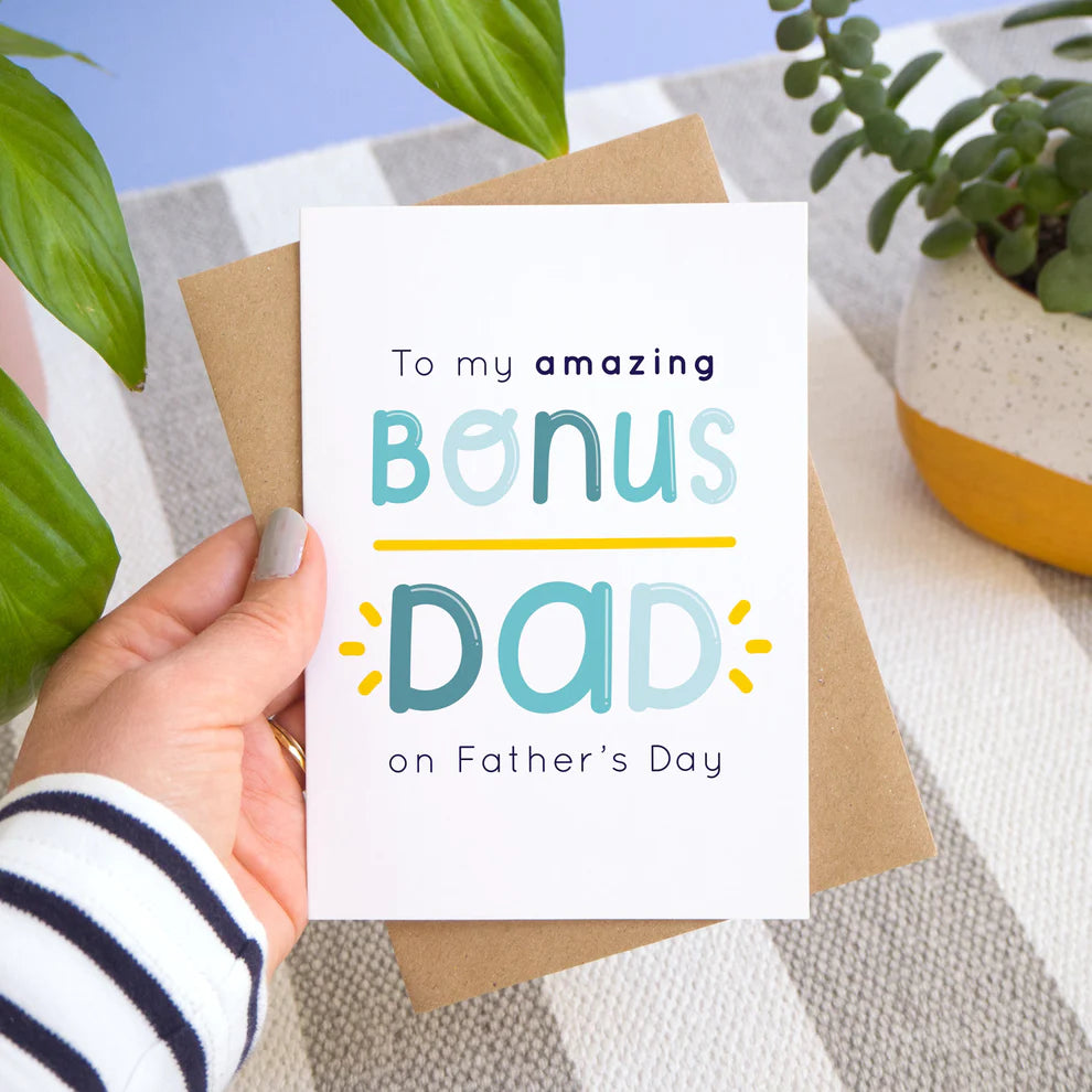 Bonus dad father's day card for step dads held over a striped surface amongst pot plants.