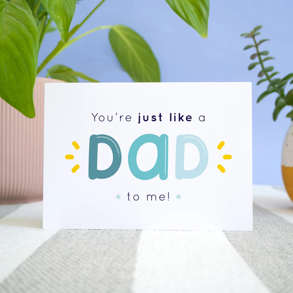 Like a dad to me card stood in front of a blue background and potted plants.