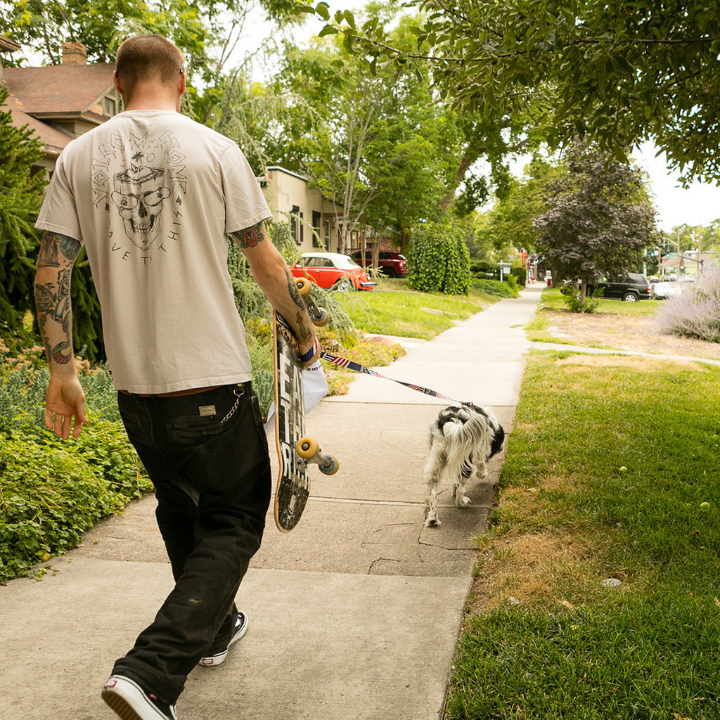 Pat Moore walking on a sidewalk with his dog Murphy carrying his skateboard.