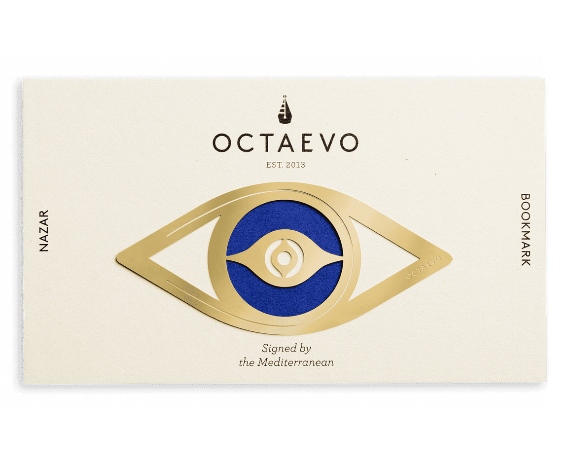 A white packaging card with a blue circle aligns with the circle of the brass bookmark that is an outlined shape of the Nazar eye.