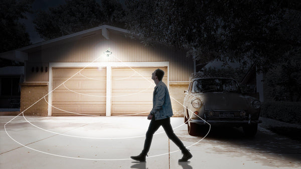 male figure walking in front of a driveway at night lit up by the Outdoor Motion Flood Light by STKR Concepts