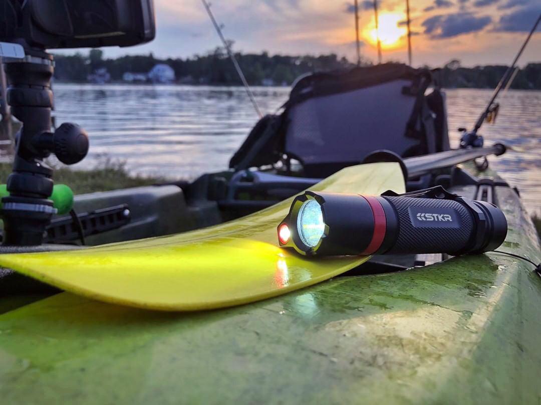 BAMFF Tactical Flashlight sitting on a fishing kayak that is beached. Sunset lake scene in the background.