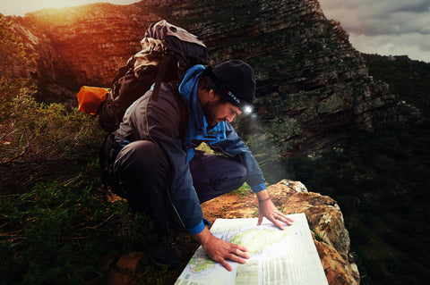 Hombre caminando por las montañas con un faro STKR arrodillado y mirando un mapa en el suelo